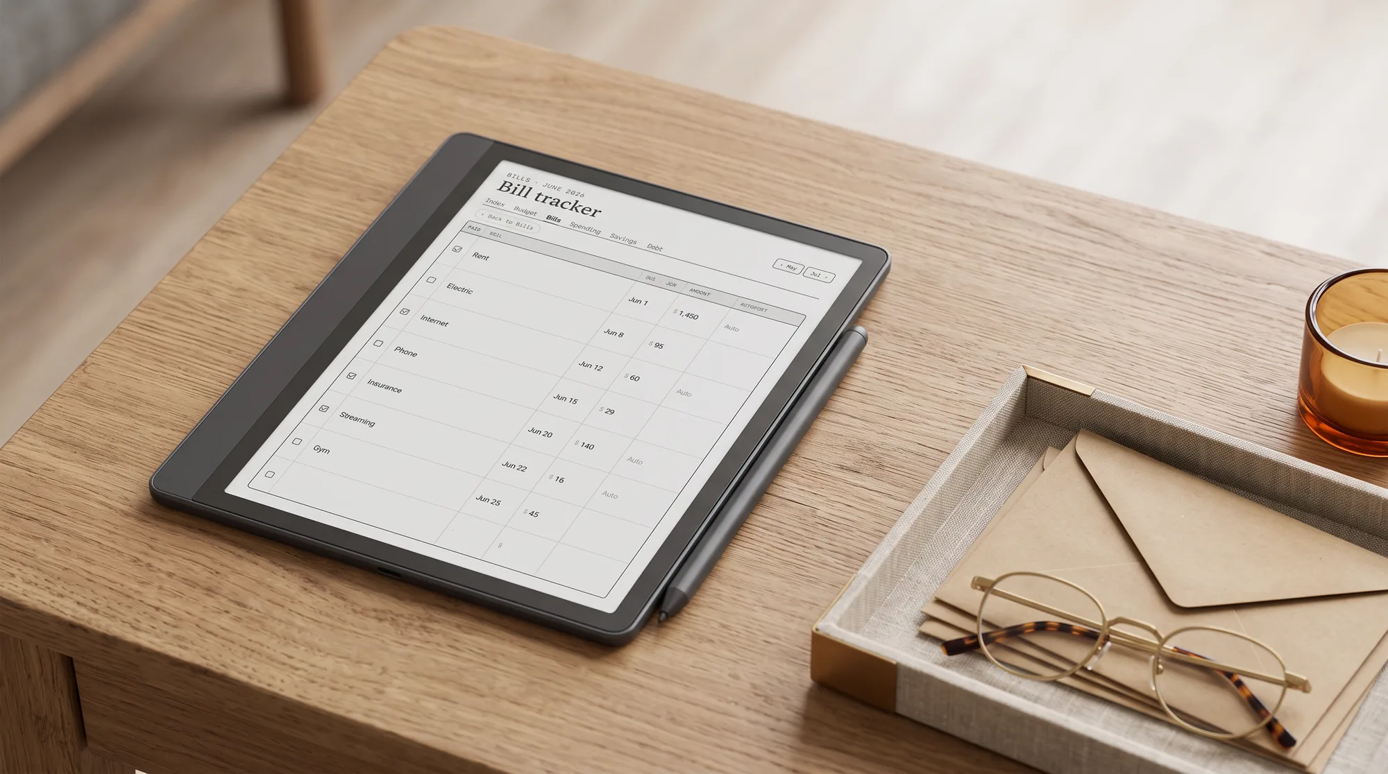 A Kindle Scribe showing a bill tracker, laid on a desk with a tray of envelopes and reading glasses
