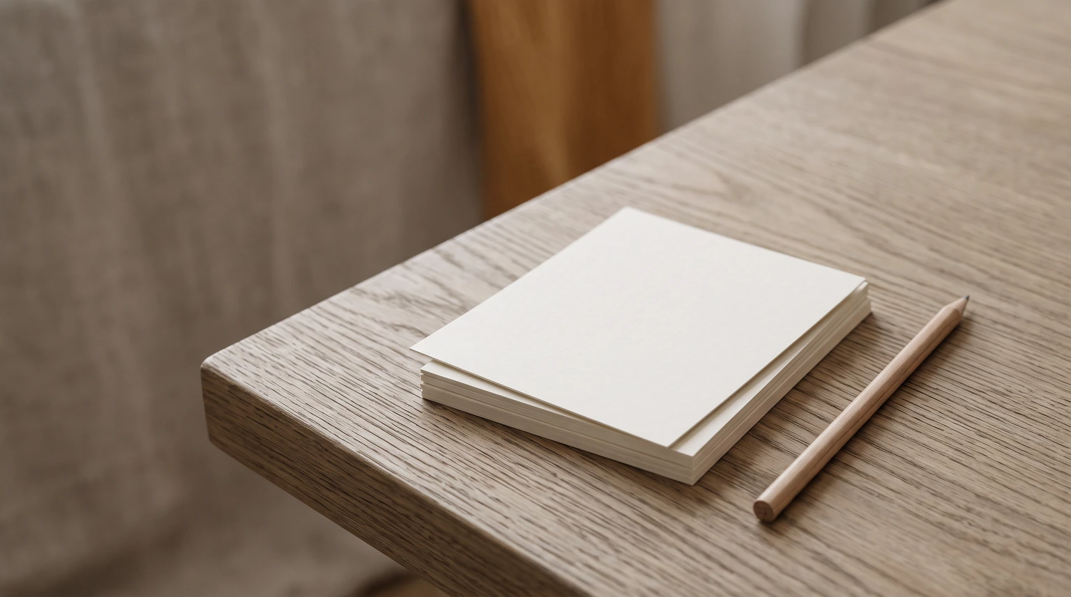 A small stack of blank note cards and a pencil on a wooden desk